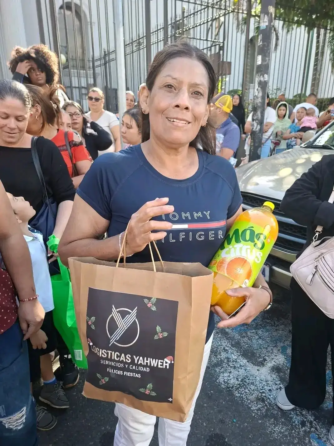 Mujer sostiene una bolsa con el logotipo de Logísticas Yahweh y la leyenda «Felices Fiestas», junto a una botella de refresco