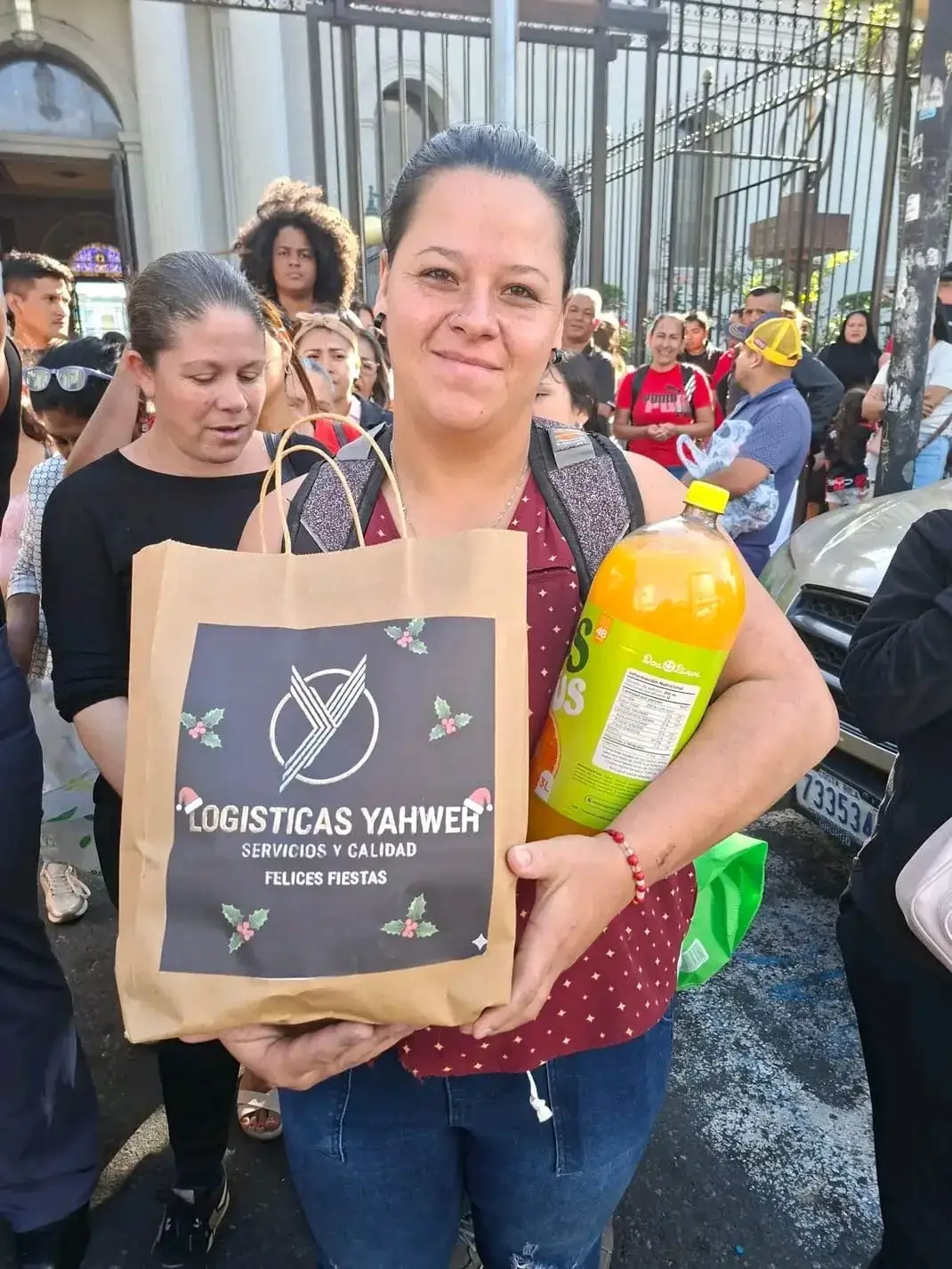 Mujer sonriendo con la bolsa de «Felices Fiestas» de Logísticas Yahweh, rodeada de otras personas