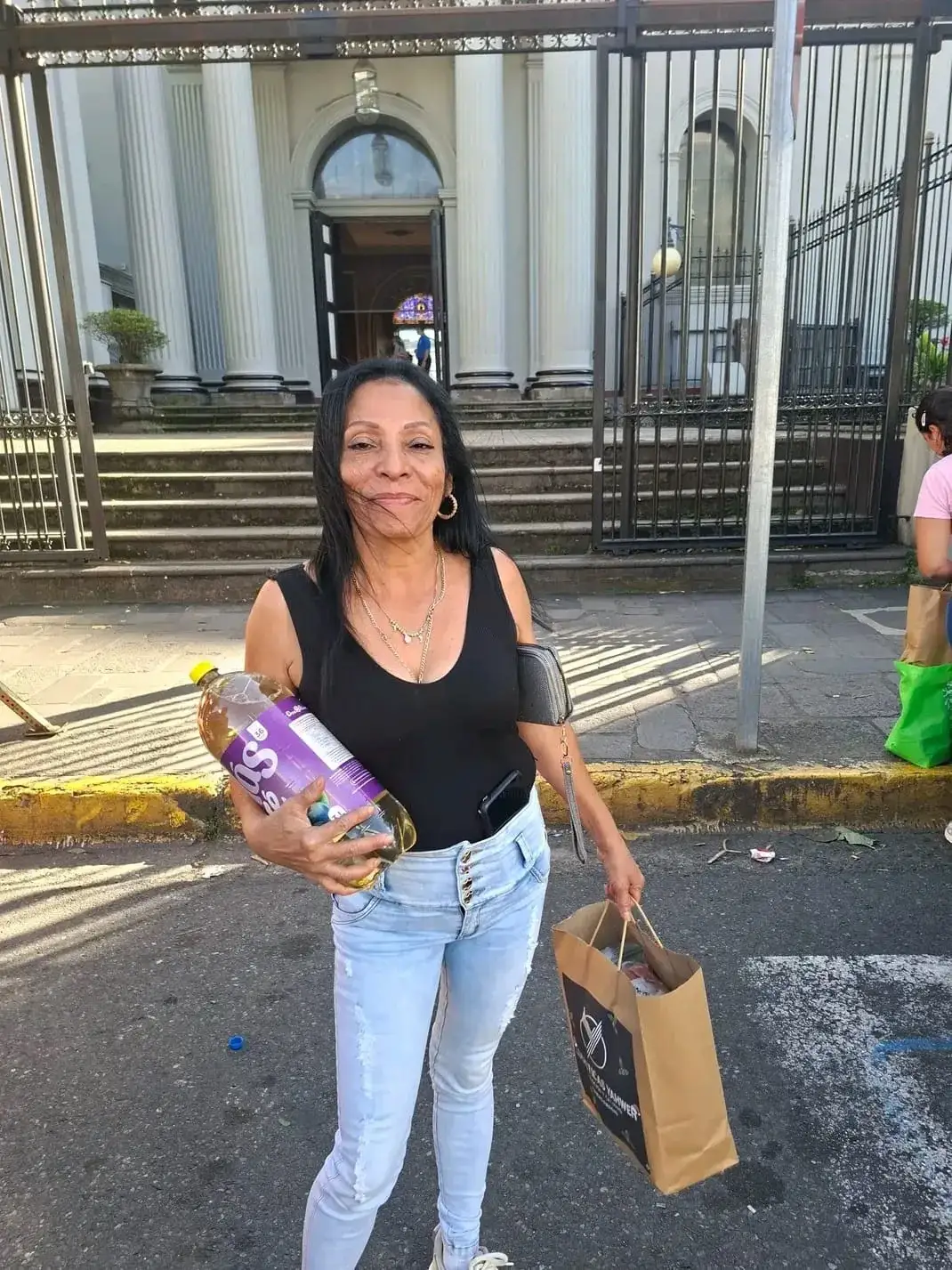 Mujer con una bolsa de Logísticas Yahweh y una botella de refresco, frente a una iglesia