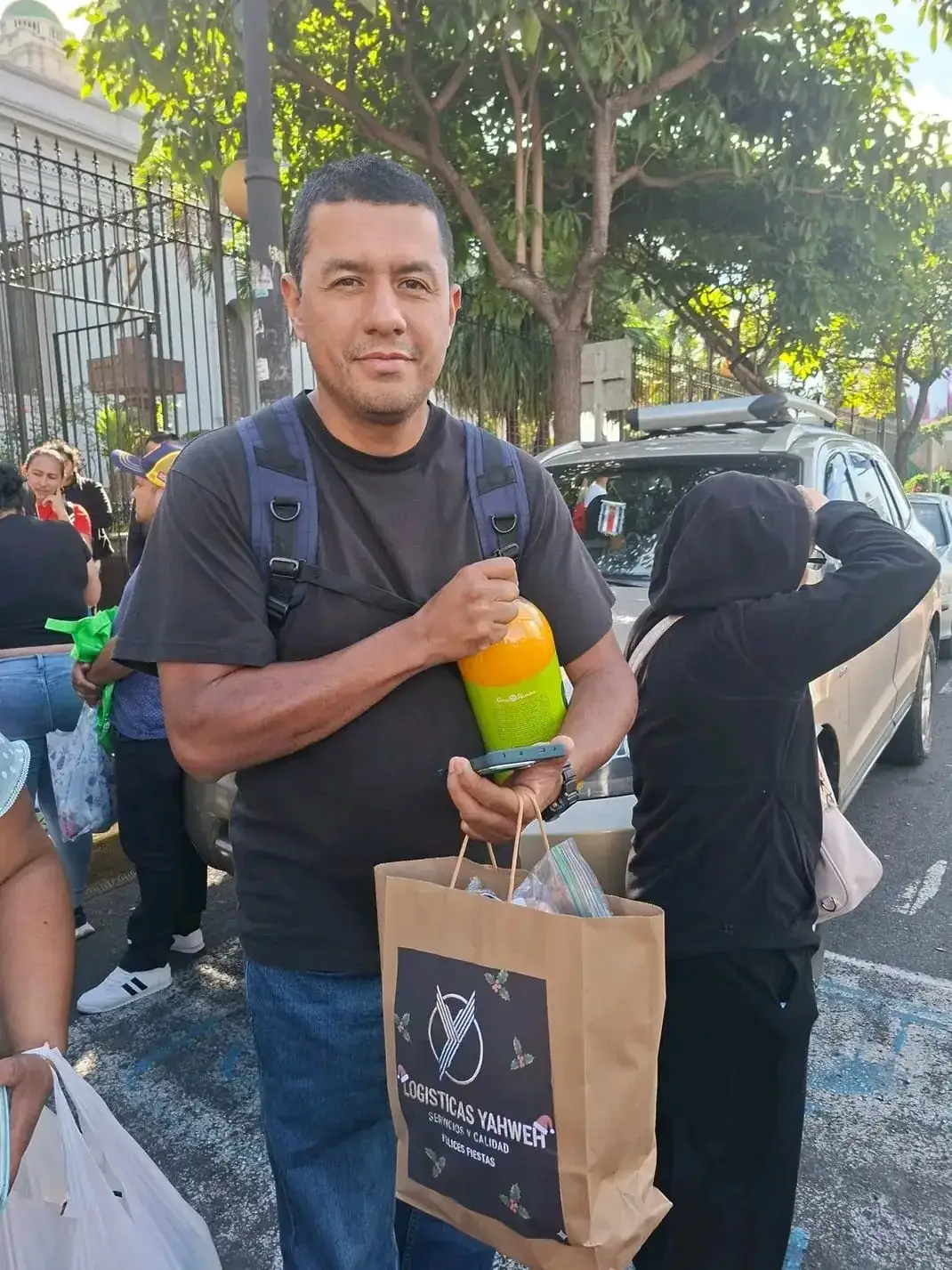 Persona sostiene la bolsa de «Felices Fiestas» de Logísticas Yahweh junto a una botella de refresco